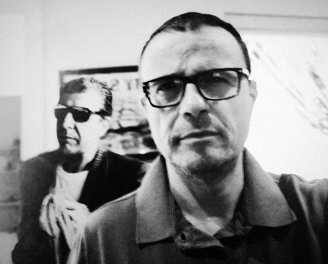 Artur Rodríguez en blanco y negro, con un retrato de Leonard Cohen detrás